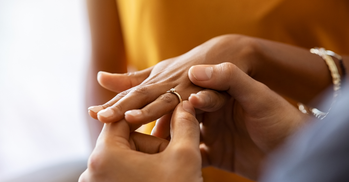 Close-up of a man placing a ring on a woman’s finger, symbolizing love and marriage for Kind Wealth’s article on pre-nups.